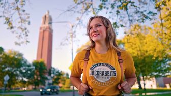 Female student walking on South Dakota State University Campus with a campanile in the background.