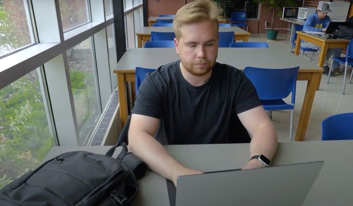 Male student typing on his computer in a study space on campus.